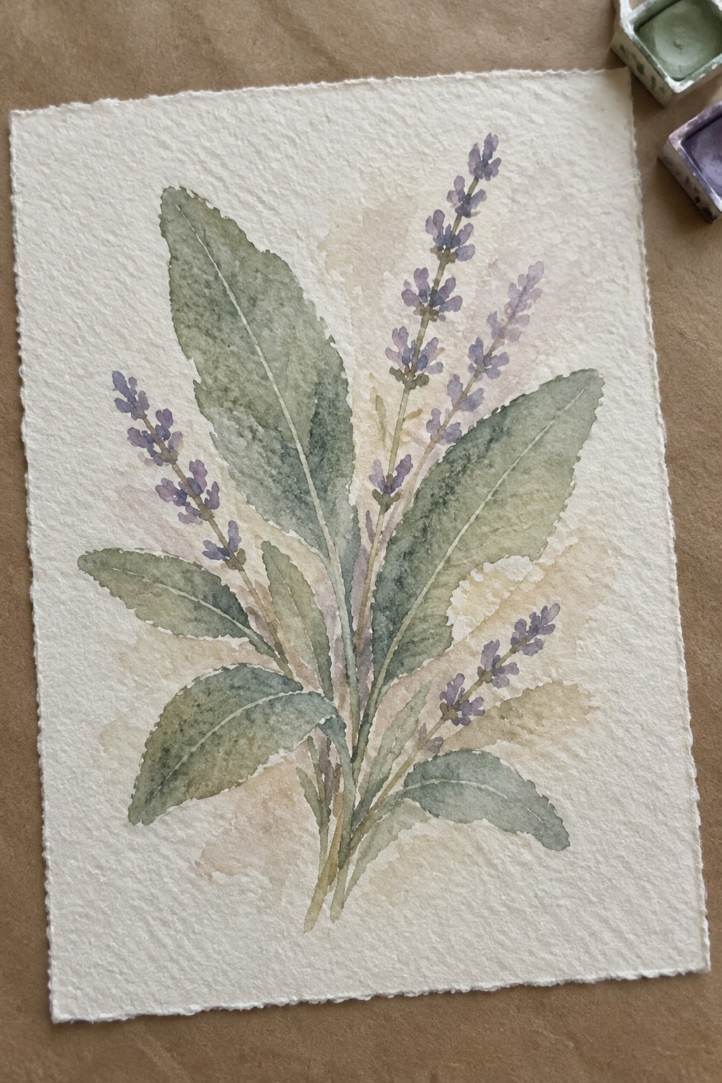 Watercolor painting of purple lavender stems with green leaves on textured paper near paint sets