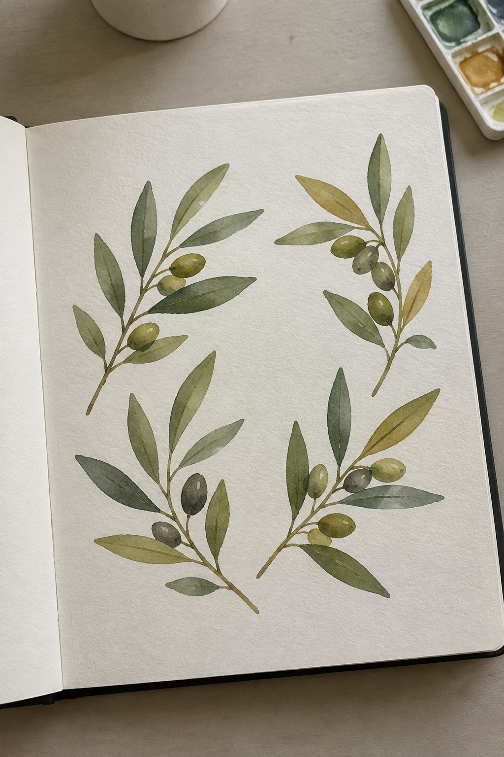 Open sketchbook with four watercolor olive branch paintings and nearby palette.