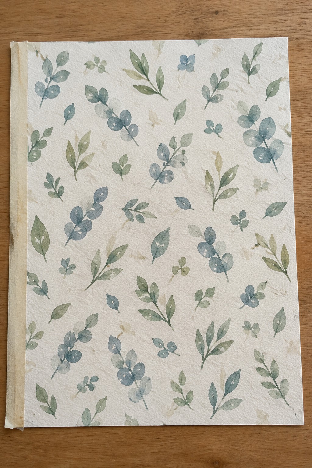 Watercolor botanical pattern of blue-green leaves on textured white paper over wood