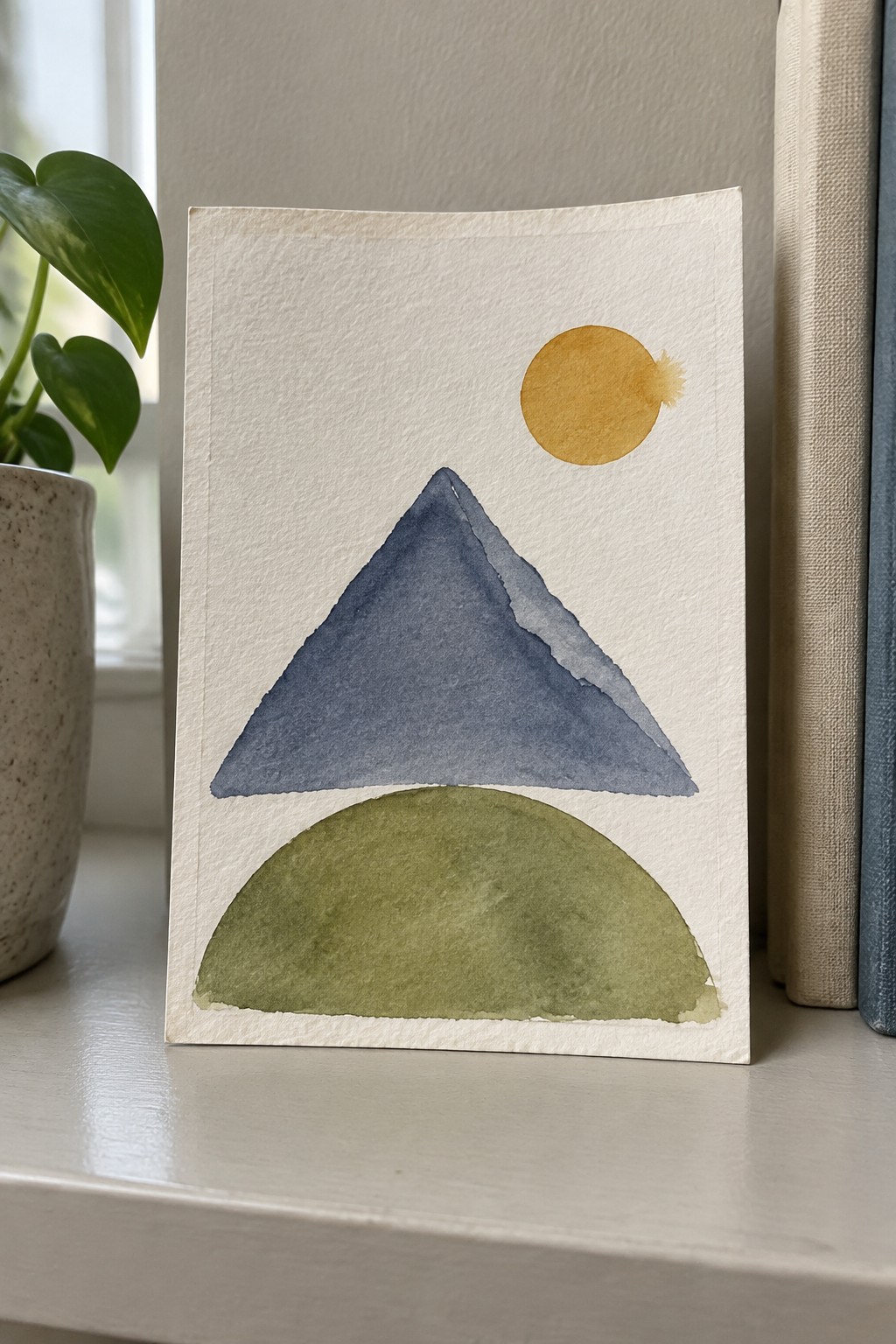Watercolor abstract of blue mountain, green semicircle, and yellow sun on paper.