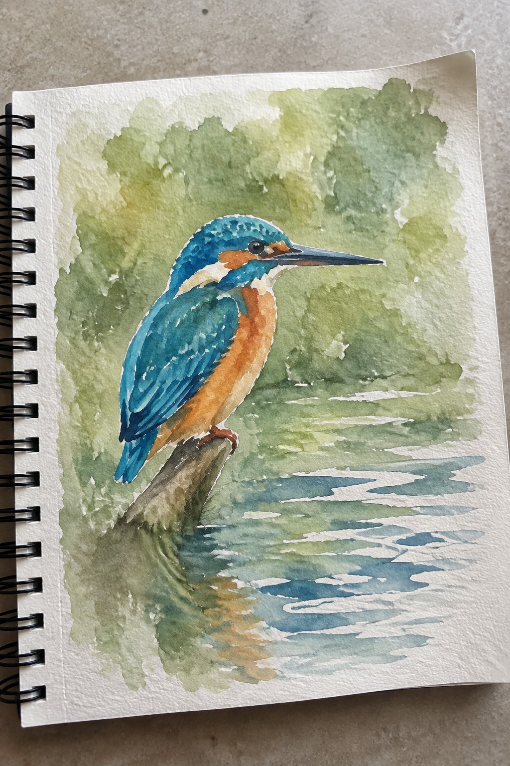 Watercolor painting of blue-orange kingfisher perched on branch above rippling water in sketchbook.