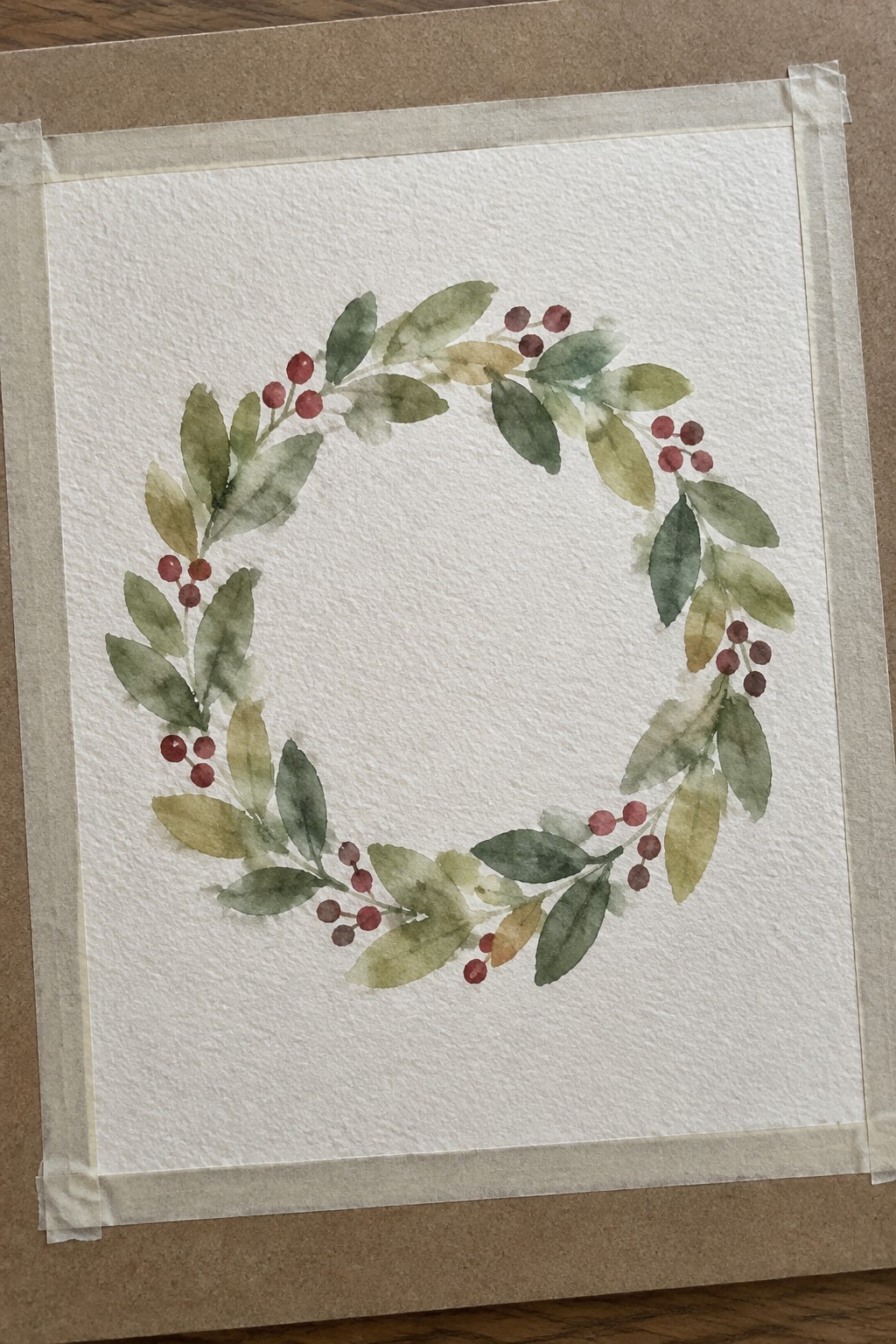 Watercolor wreath of green leaves and red berries on taped white paper