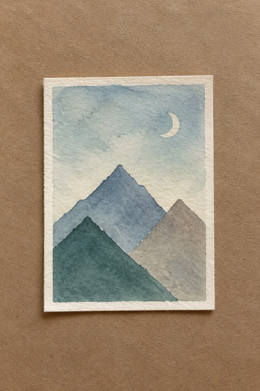 Watercolor painting of layered blue mountains with crescent moon in soft sky