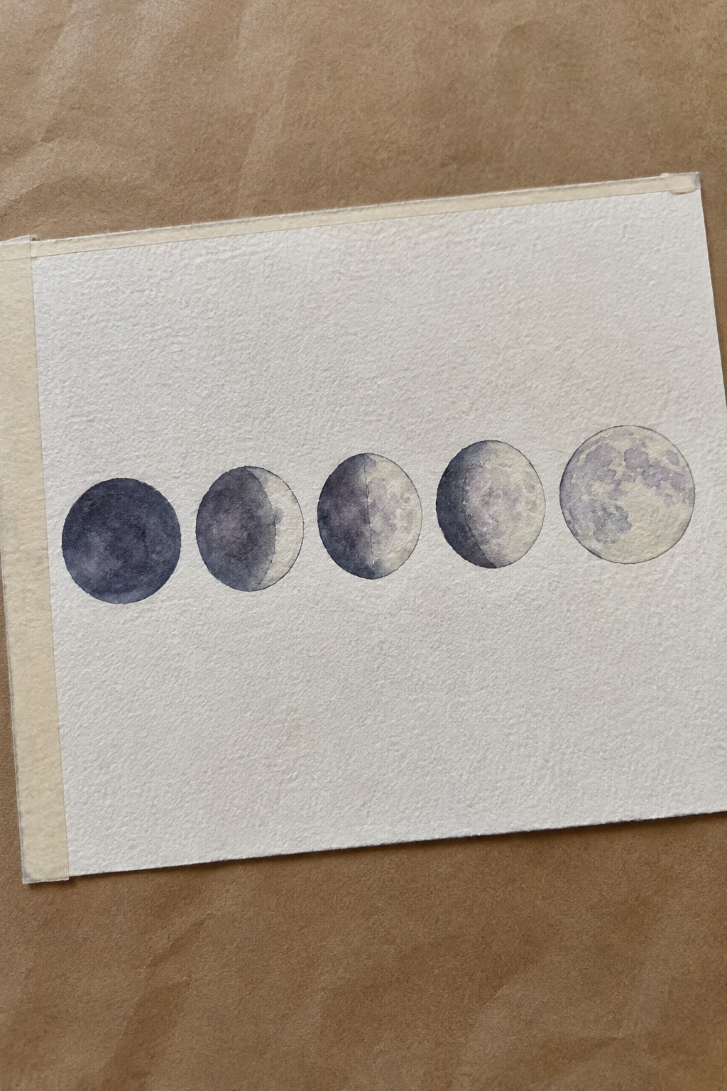 Watercolor painting of five moon phases in a row on textured white paper