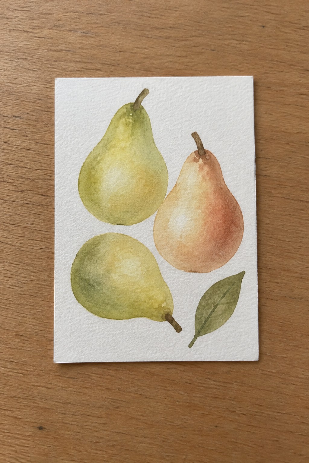 Watercolor painting of three green, yellow, and orange pears with a leaf on white paper