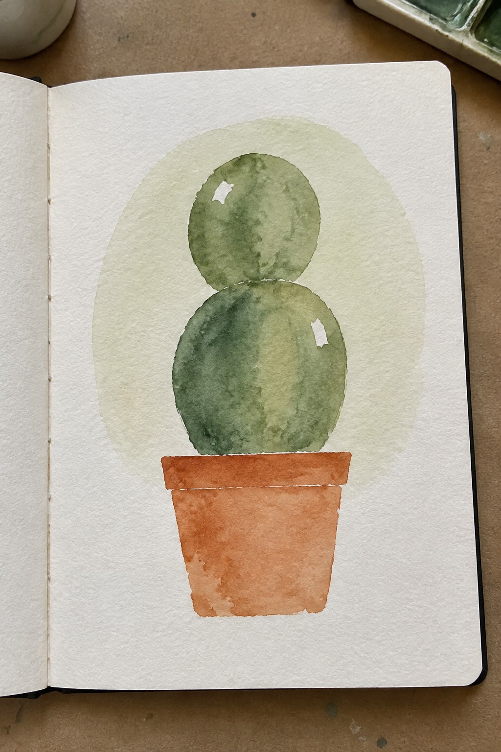 A watercolor painting of a green stacked cactus in an orange pot with a light green oval wash behind it on white paper.