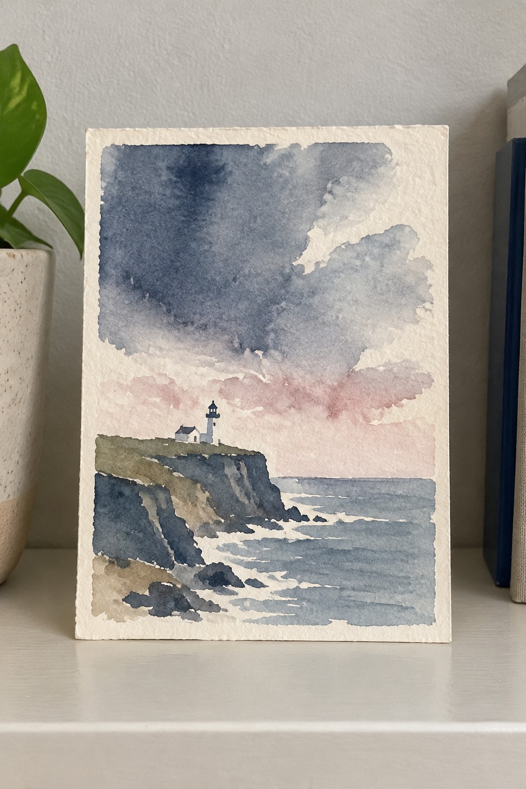 Watercolor painting of lighthouse on rocky cliff overlooking stormy sea with pink clouds