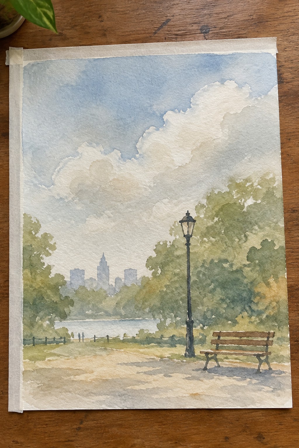 Watercolor of park bench, lamppost, path, trees, water, and distant city skyline under clouds