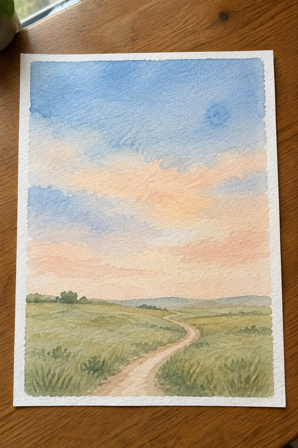 Watercolor landscape of winding path through green fields under colorful sunset sky.