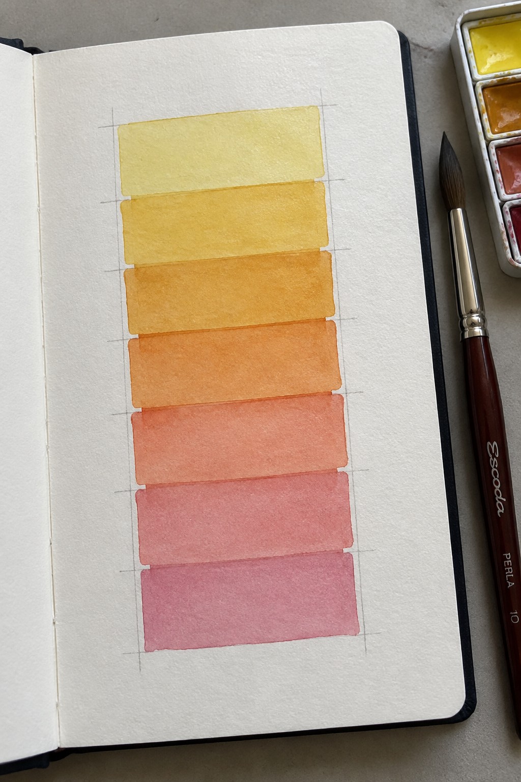 Open sketchbook with yellow-to-pink watercolor gradient swatches beside paintbrush and palette.