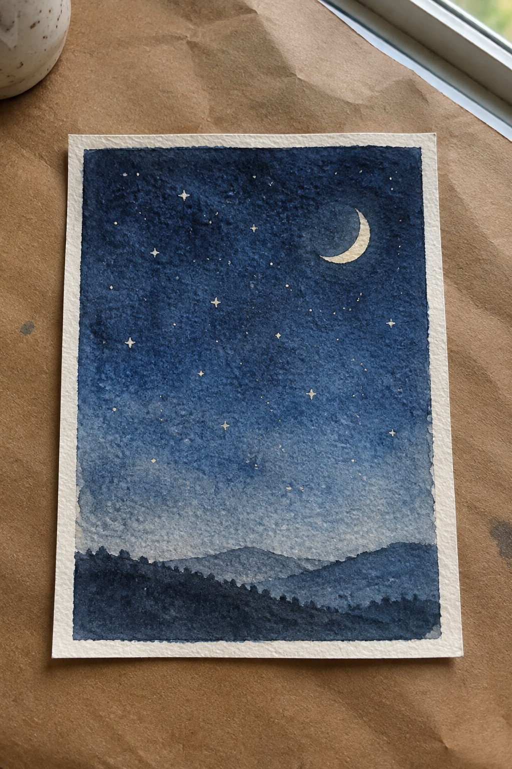 Watercolor night sky with stars, crescent moon, and silhouetted mountains in blue tones
