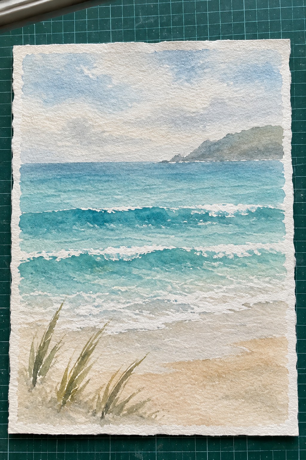 Watercolor painting of blue-green waves breaking on sandy beach with grass and distant hills