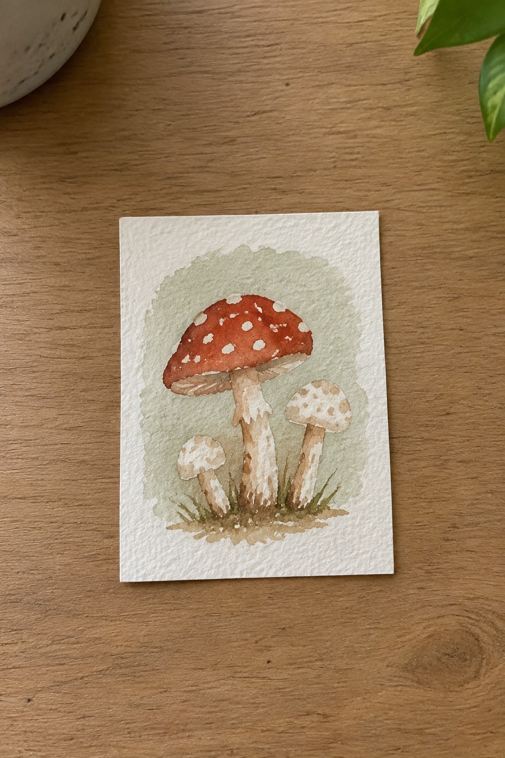 Watercolor of red and white spotted mushrooms with smaller beige ones on wood