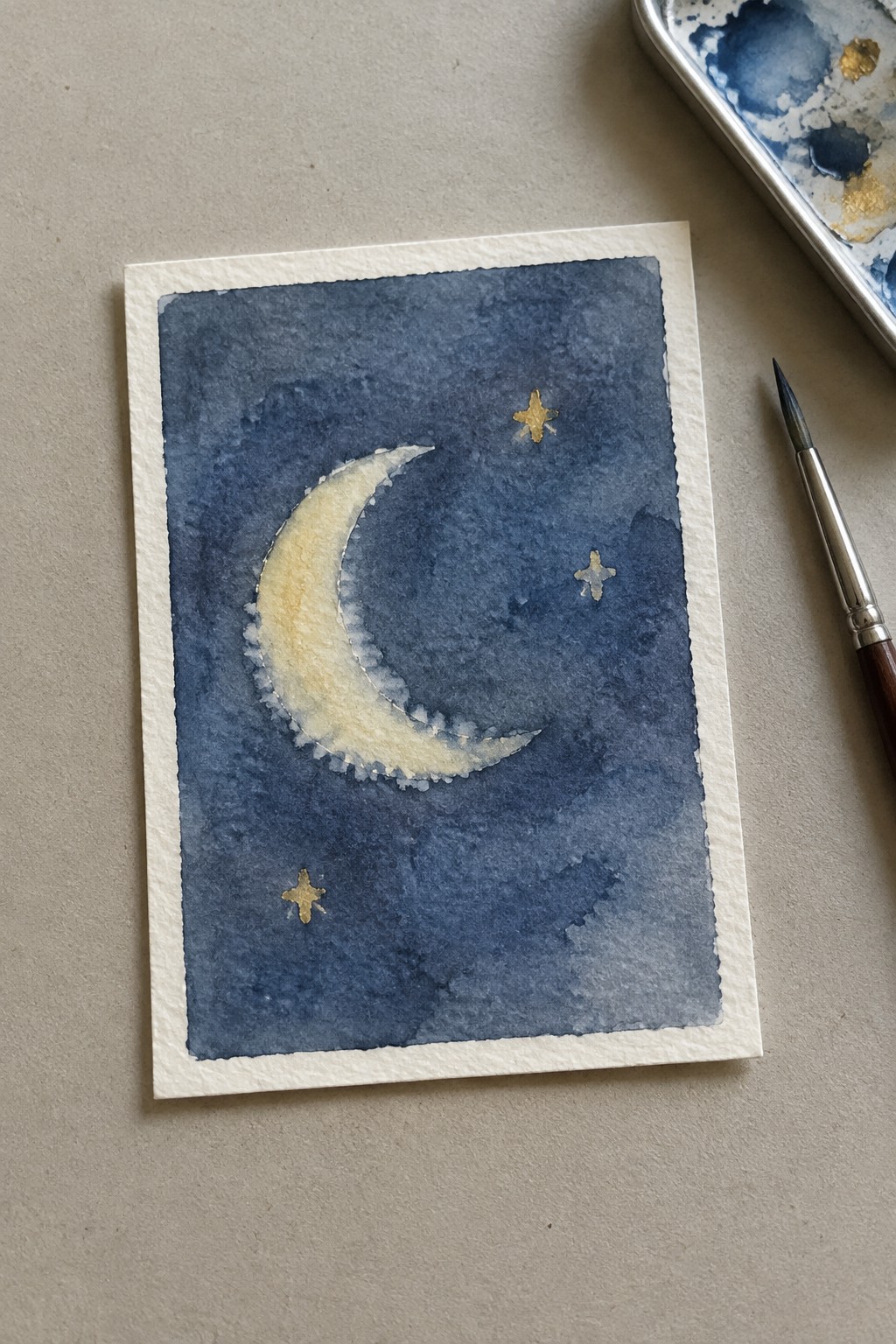 Watercolor painting of yellow crescent moon with gold stars on dark blue sky