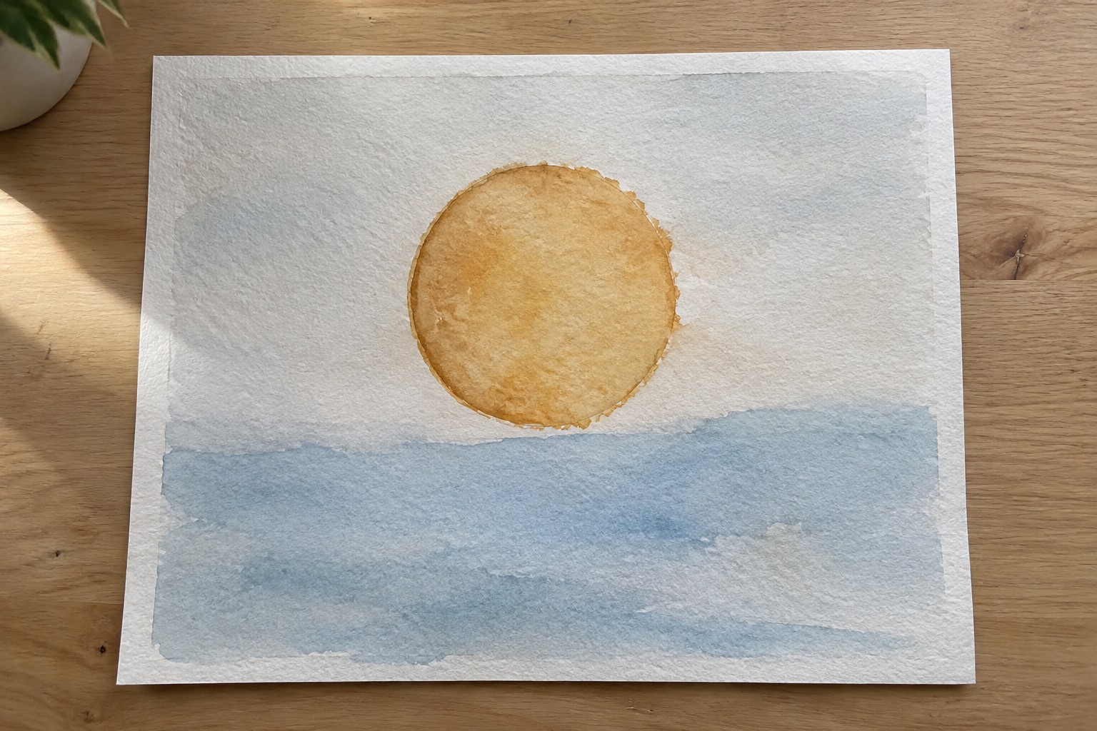 Watercolor painting of an orange sun circle above a light blue horizontal wash on white paper.