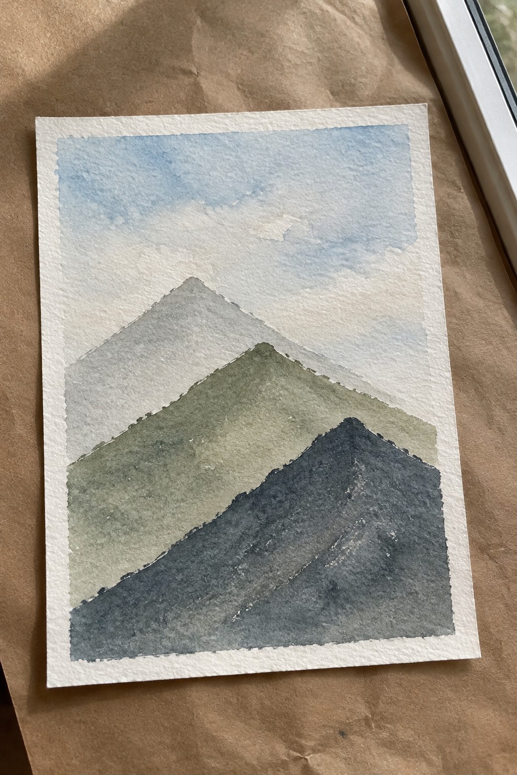 Watercolor painting of layered mountains in green, gray, and blue with soft sky