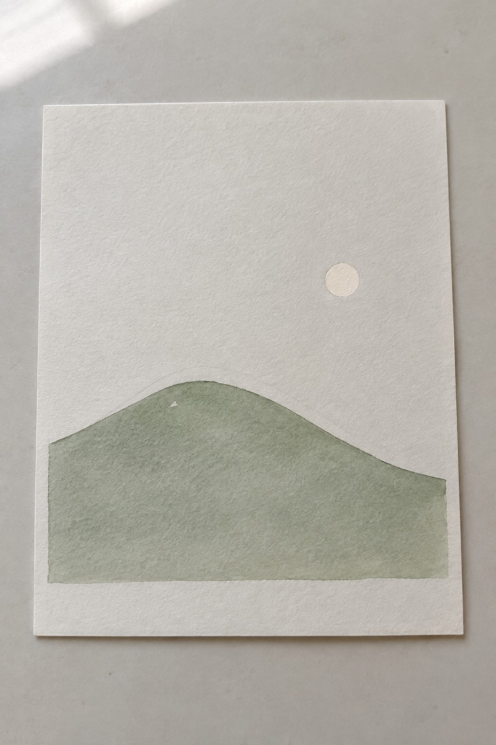 Minimalist watercolor of green hill with faint outline and small white circle above.
