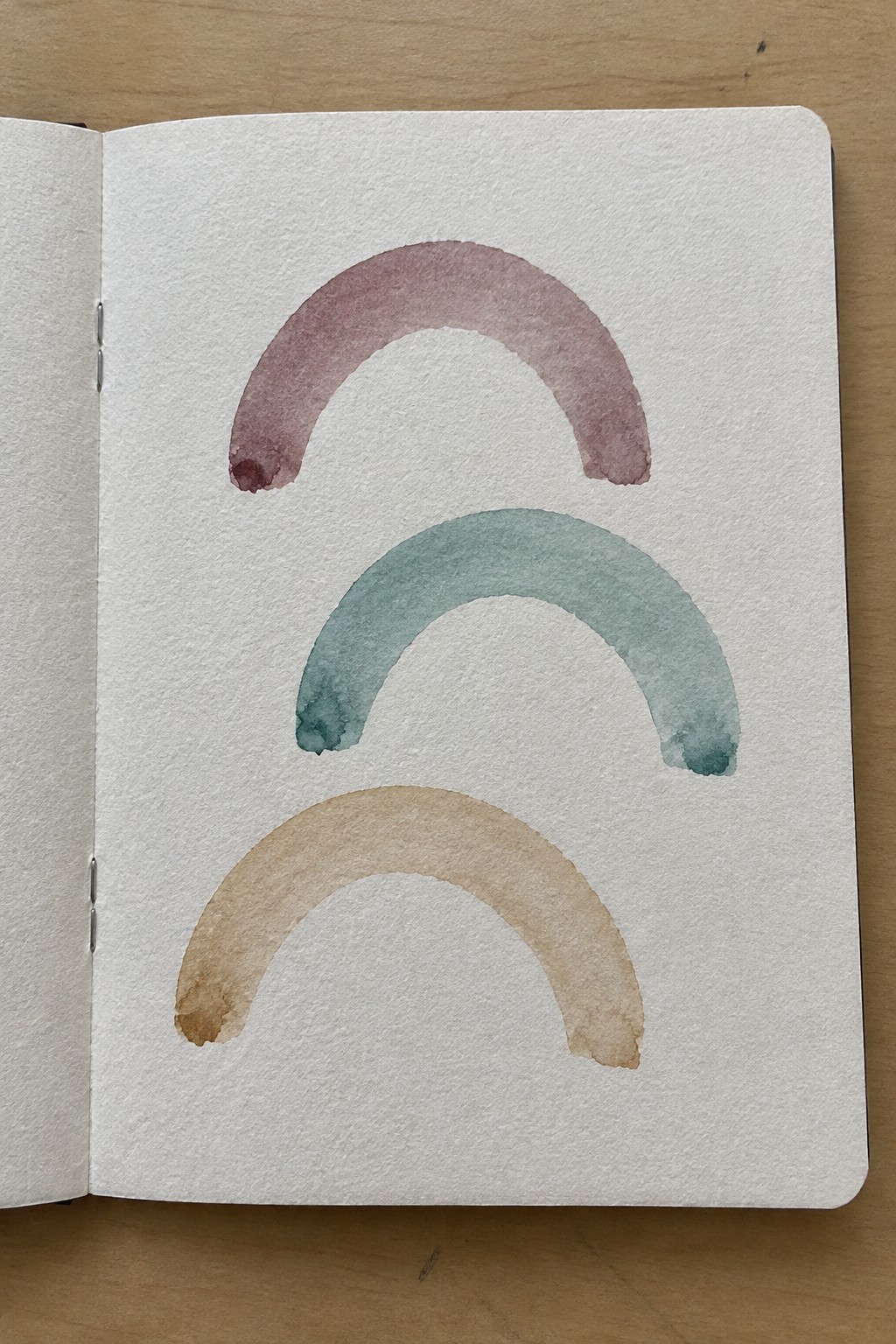 Open sketchbook page with three stacked watercolor arcs in pink, teal, and tan.