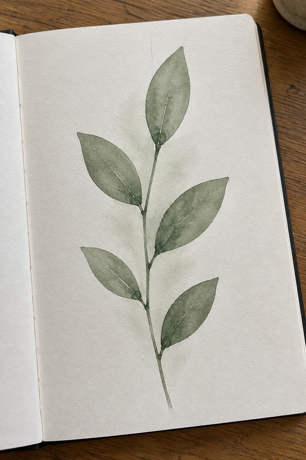 Watercolor green leafy branch painted in open notebook on wooden table