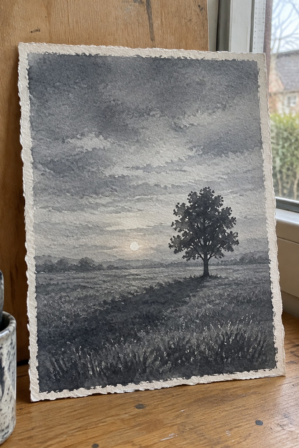 Watercolor landscape of lone tree in field beneath cloudy sky with low sun.