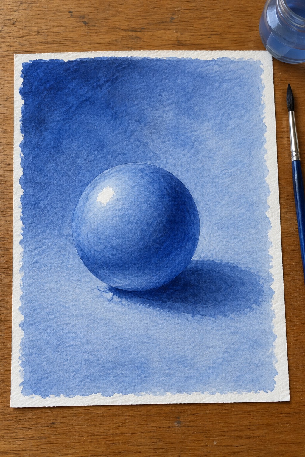 Watercolor blue sphere with soft shadow on textured paper beside paintbrush and jar on wood