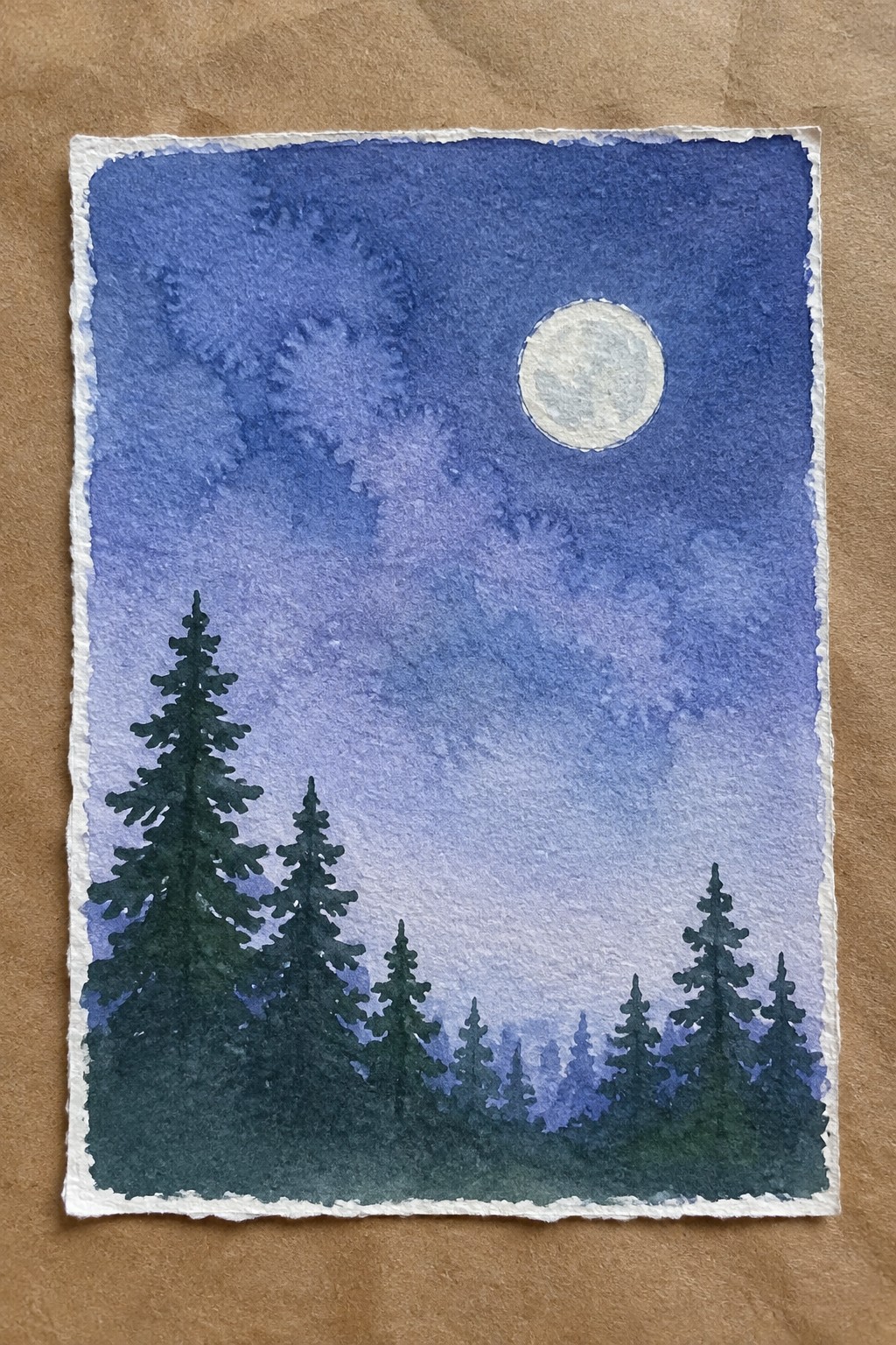 Watercolor of full moon in blue-purple sky above silhouetted pine trees on textured paper