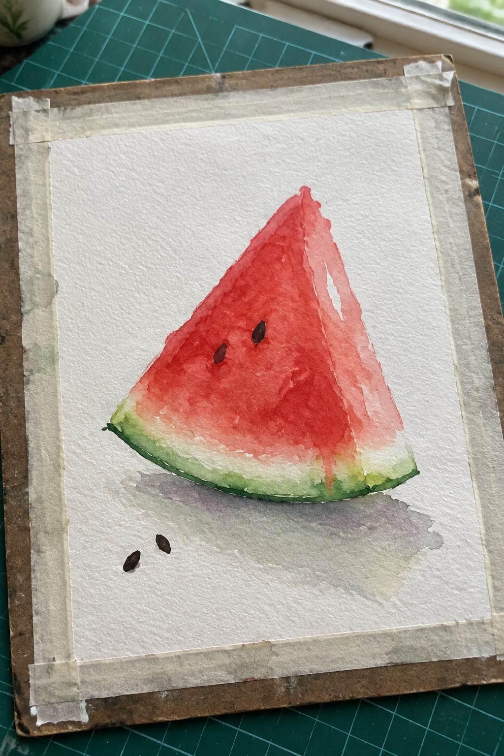 Watercolor of watermelon slice with red flesh, green rind, seeds on taped white paper