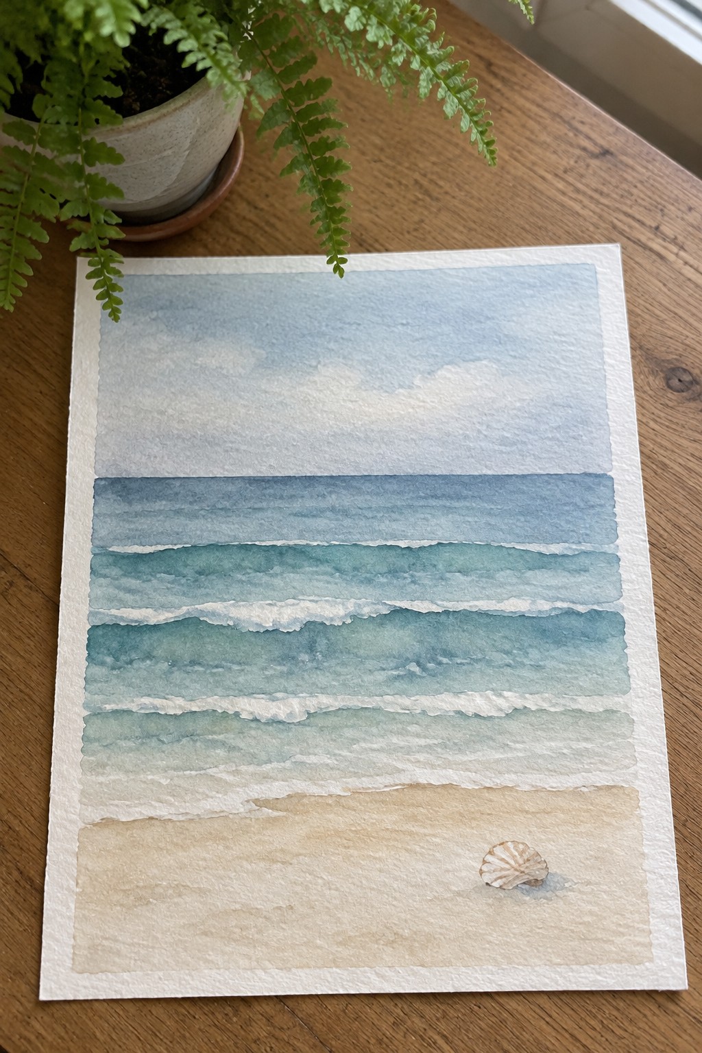 Watercolor seascape of blue waves on sandy beach with seashell beside potted fern on wood