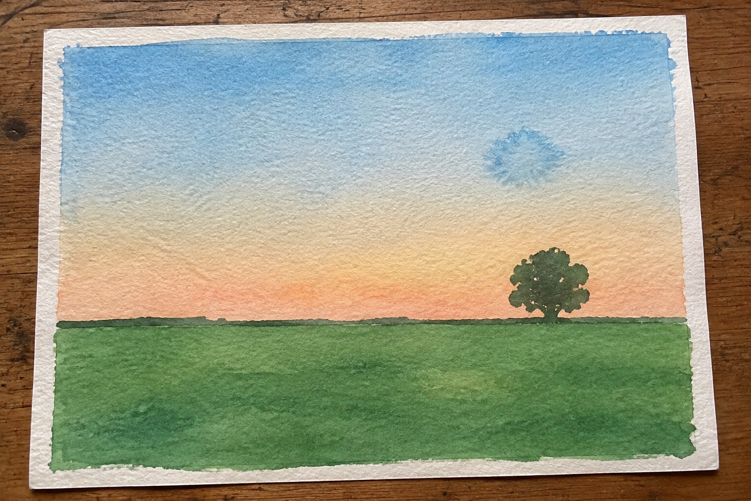 Watercolor landscape of green field with lone tree under blue-orange sunset sky