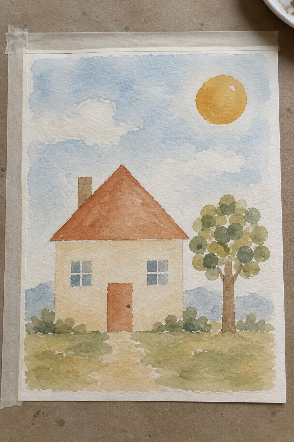 A watercolor painting of a beige house with an orange roof, chimney, door, and two windows, a path leading to it, a leafy tree, bushes, a yellow sun, and blue sky with clouds over distant hills.