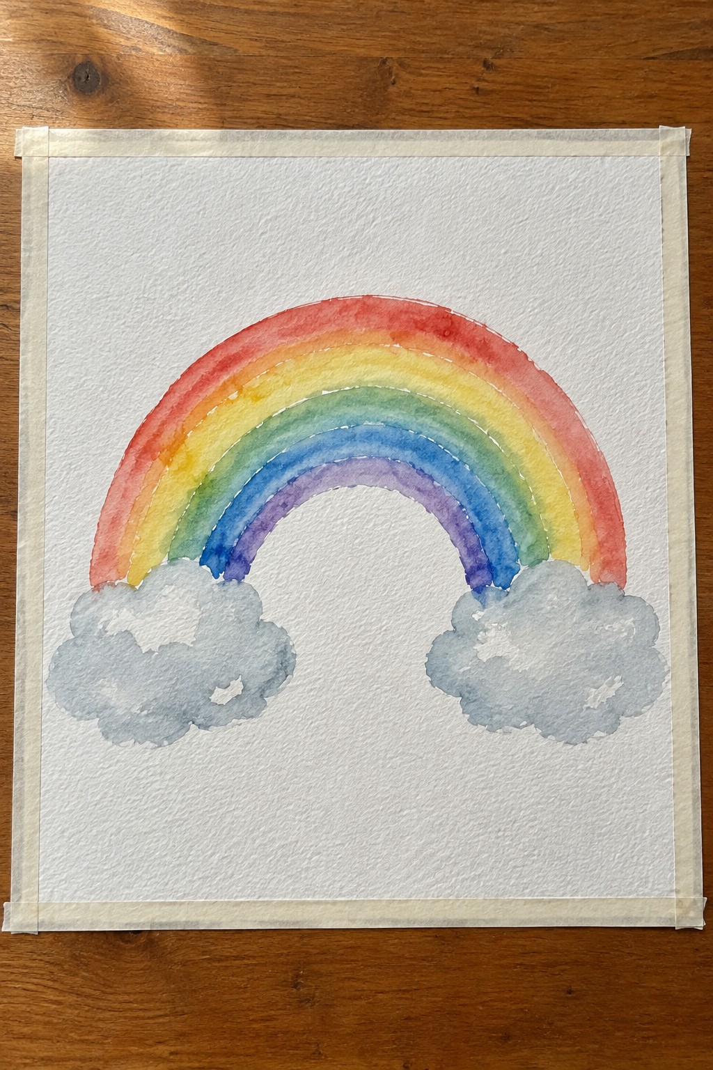 Watercolor rainbow with red-orange-yellow-green-blue-purple bands and gray clouds on taped paper