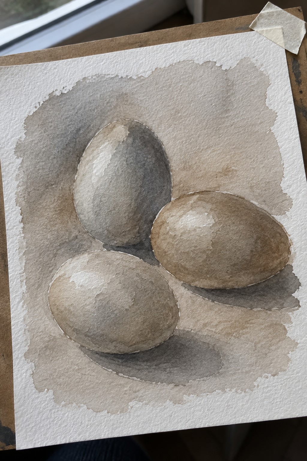 Watercolor still life of three shaded eggs on brown-washed paper with tape
