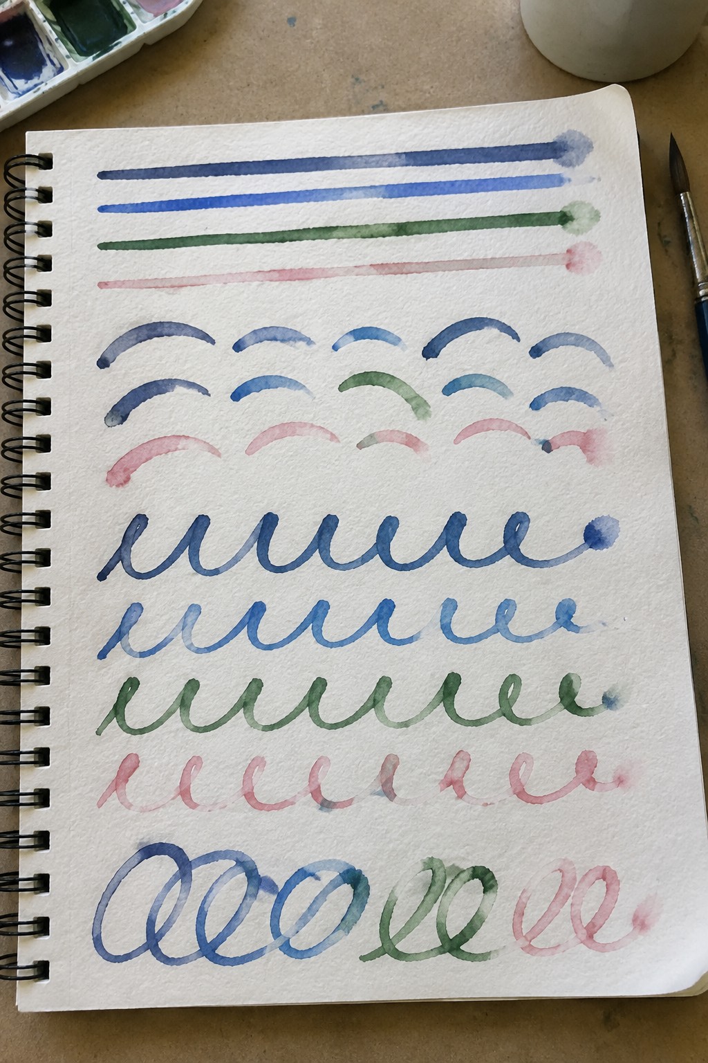 Open sketchbook with blue, green, and pink watercolor lines, curves, and squiggles