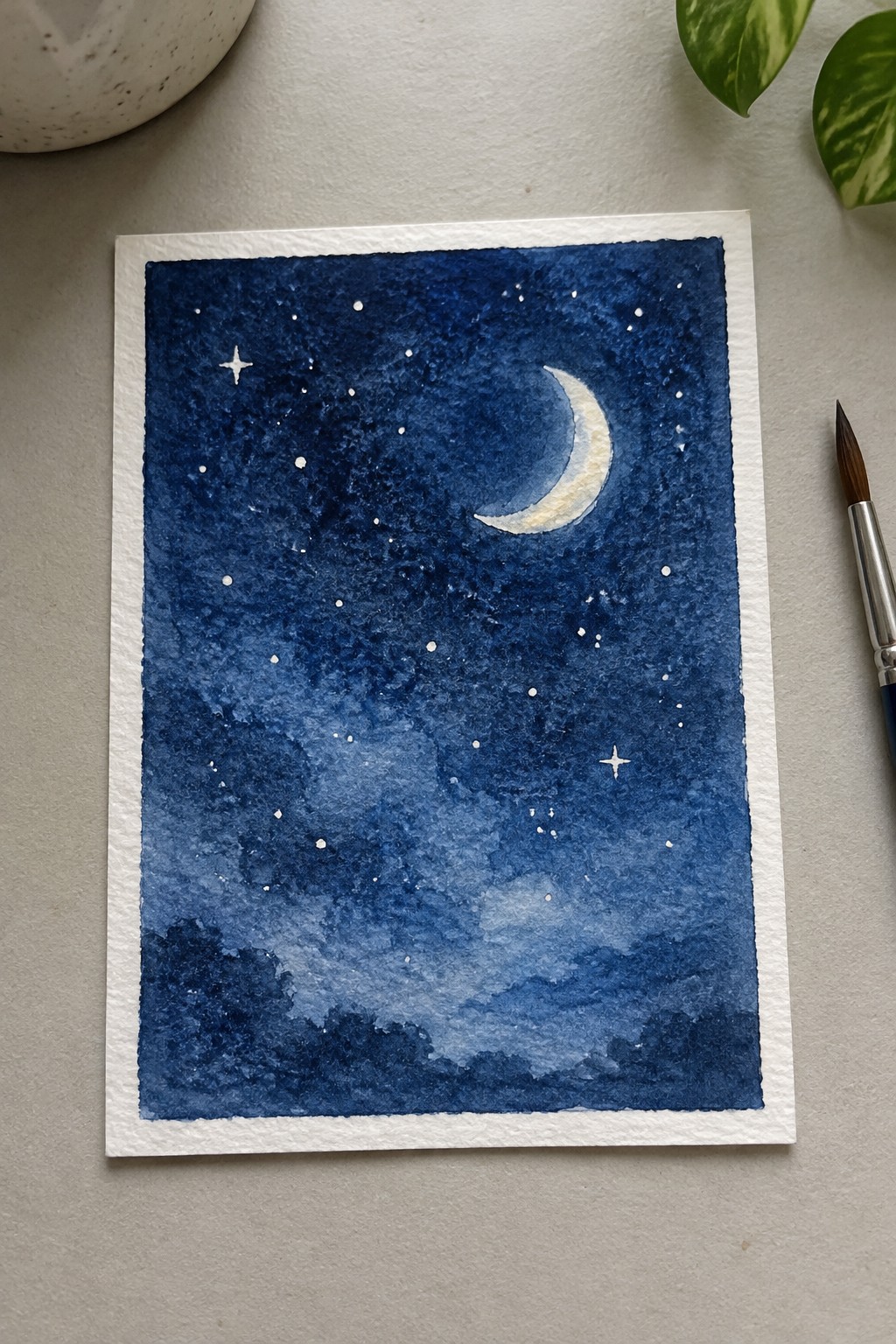 Crescent moon and stars in deep blue watercolor night sky above silhouetted trees