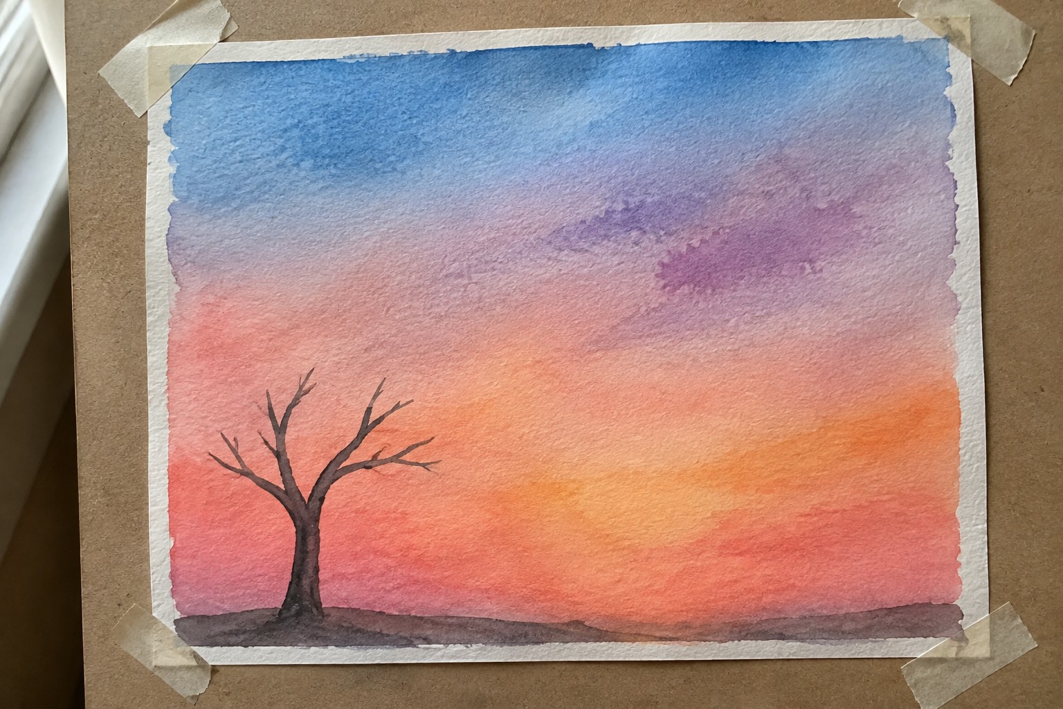 Watercolor sunset sky gradient from blue to orange with silhouetted bare tree on dark ground