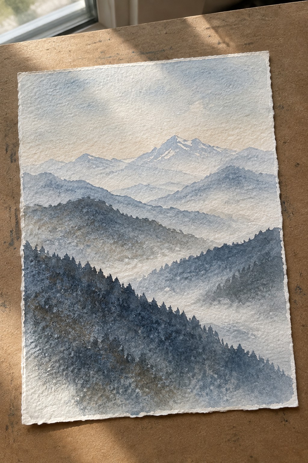 Watercolor of misty layered mountains with snow peaks above dark forested slopes on paper.