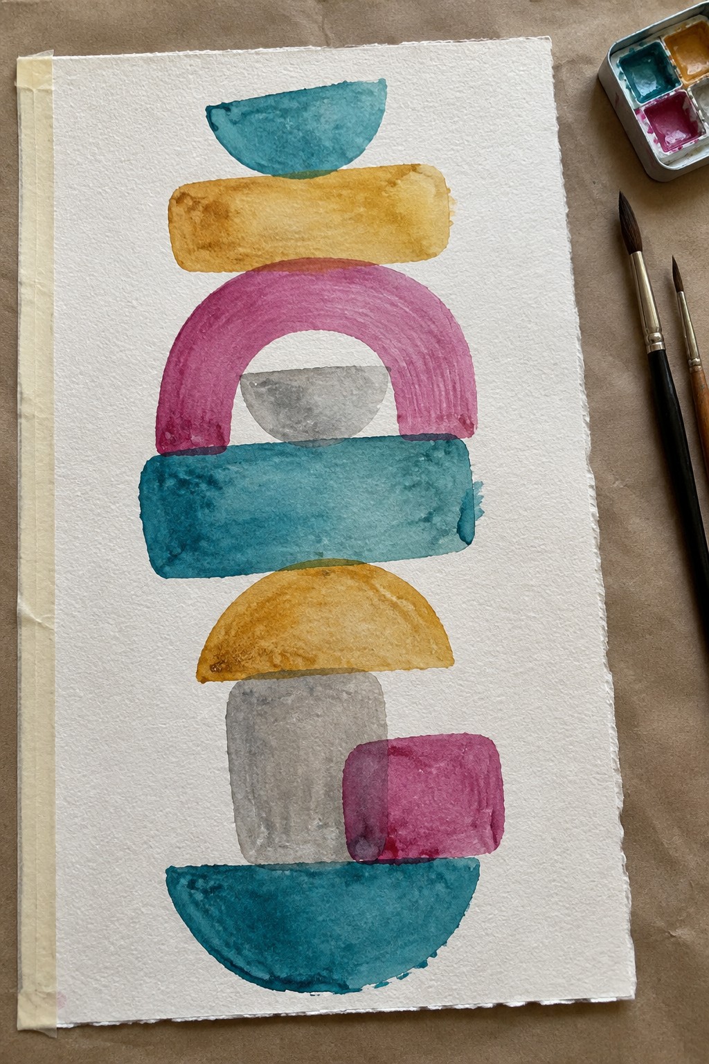 Abstract watercolor of stacked colorful shapes beside paint palette and brushes on paper