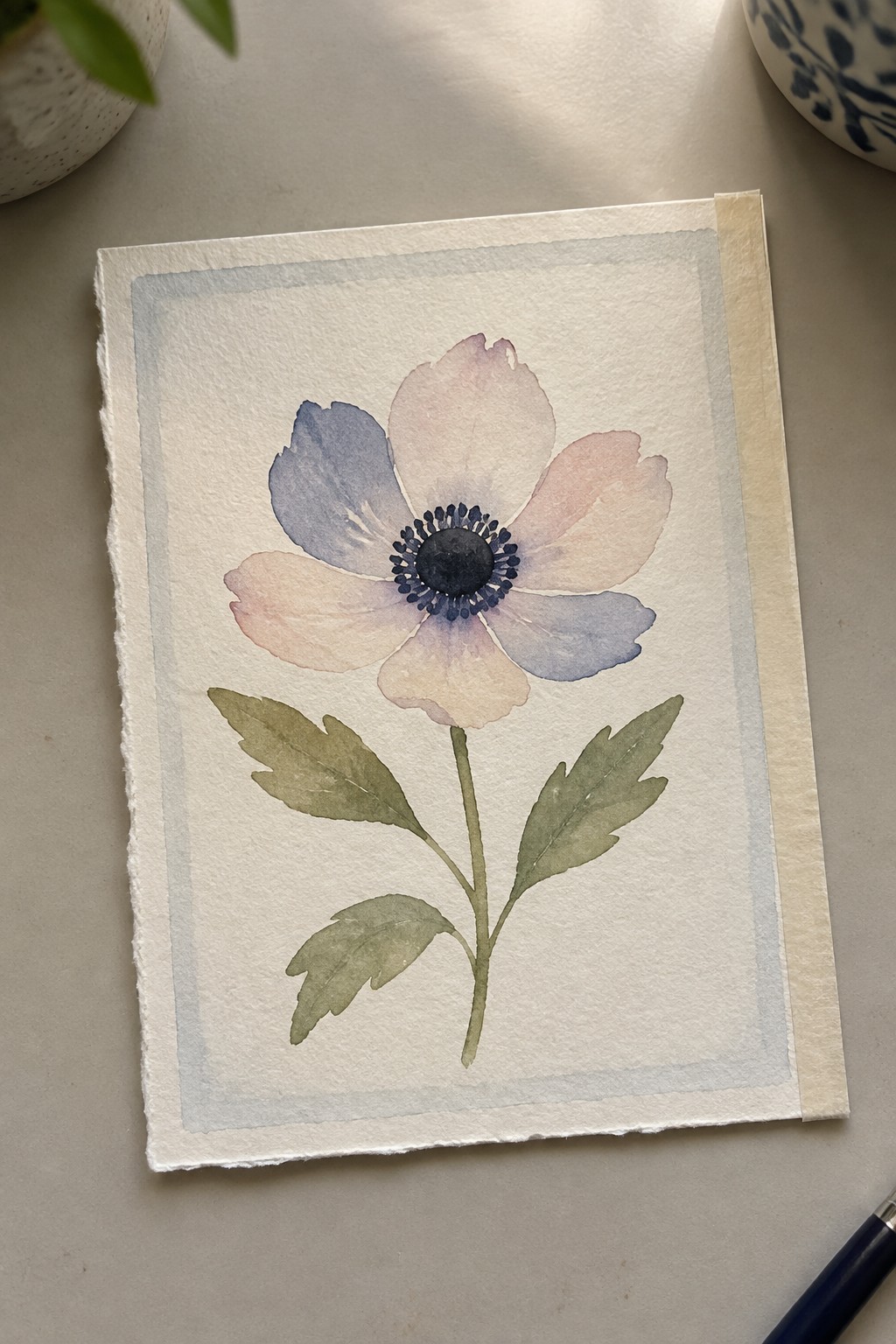 Watercolor anemone with soft blue-pink petals, dark center, and green leaves