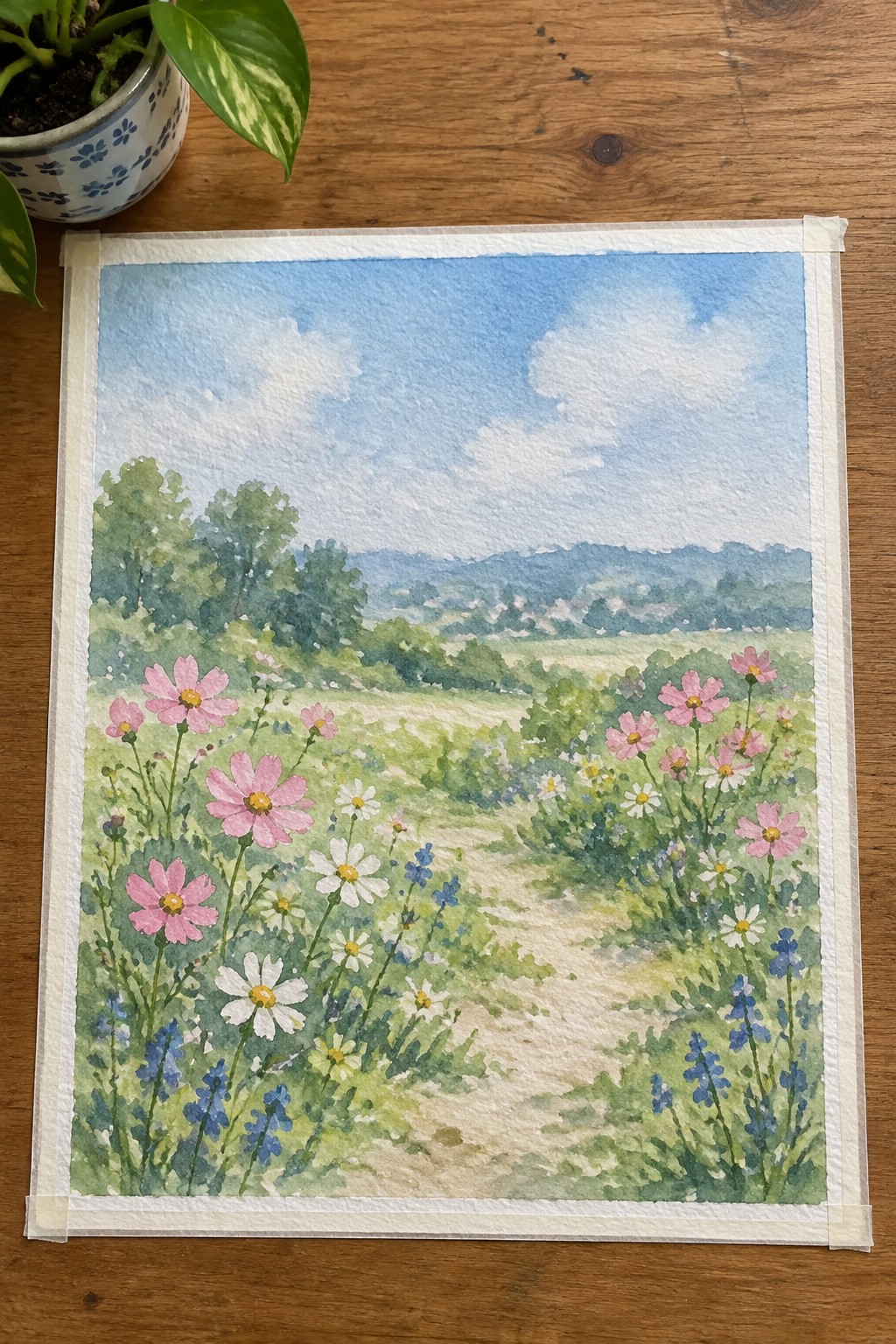 Watercolor landscape of pink cosmos, white daisies, and blue flowers along a winding path through green hills.