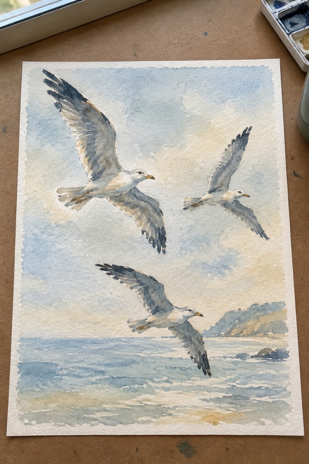 Three seagulls soar over blue ocean waves in a watercolor coastal scene.