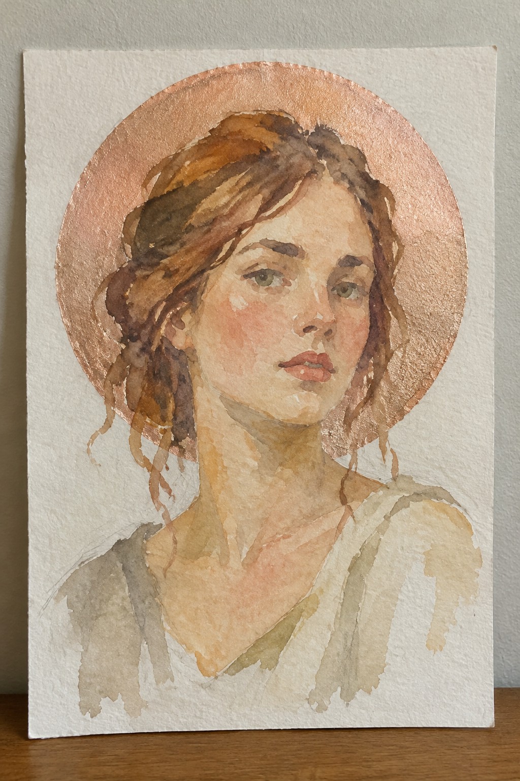 A watercolor painting of a woman's face with brown hair, set against a large copper-colored metallic circle on white paper.