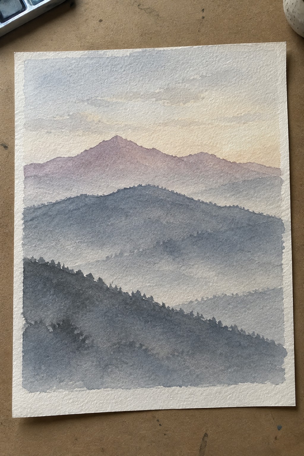 Layered blue-gray mountains with purple peaks and silhouetted trees in soft watercolor.